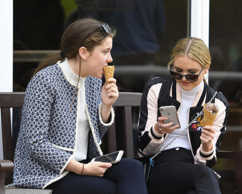 two girls eating an ice cream sat on a bench