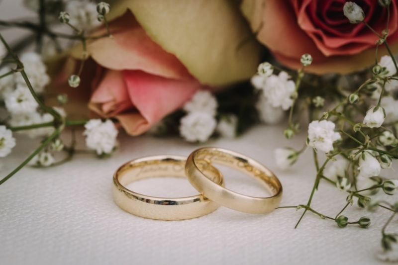 wedding rings with flowers in the background lying on table