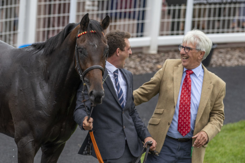 two men laughing together stood by a horse